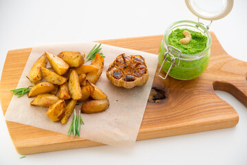 Baked potatoes with rosemary, garlic and pesto on a wooden board