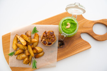 Baked potatoes with rosemary, garlic and pesto on a wooden board