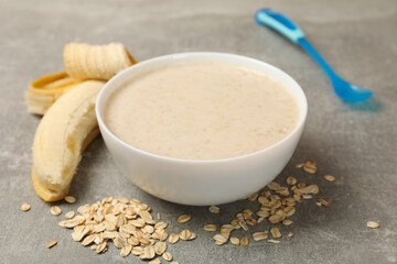 Bowl with porridge on gray background, close up. Baby food