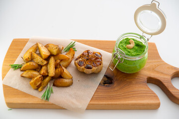 Baked potatoes with rosemary, garlic and pesto on a wooden board