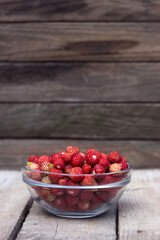 A lot of ripe wild strawberries with a clear glass plate on a wooden background. Useful red berries. Background, place for text.