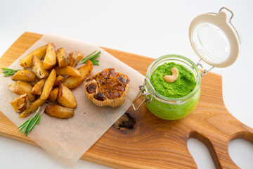 Baked potatoes with rosemary, garlic and pesto on a wooden board