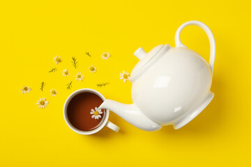 Teapot and cup of chamomile tea on yellow background, top view