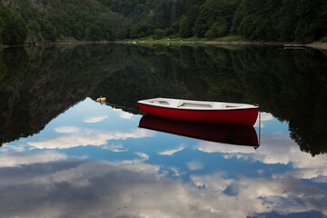 Summer lake landscape with reflections on water surface. Lake with red boat on sunny day