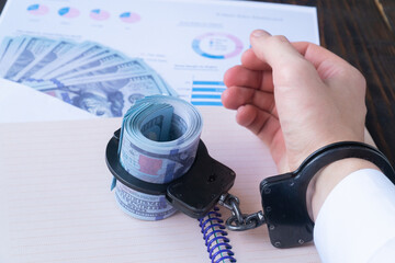 a man's hand in handcuffs, twisted dollars in handcuffs on the background of charts and money in an envelope