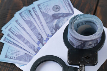 Close up twisted wad of dollars buttoned with handcuffs on wooden background, envelope with money