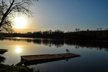 A fishing lake at sunset. Single chair on a wooden bridge made for the fisherman.