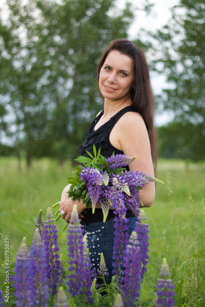 Wall mural a girl is standing in a meadow, holding a bouquet of lupine in her hands. half a turn to the camera.