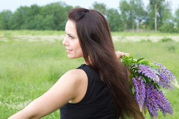 Naklejka premium A girl in jeans is half a turn to the camera, holding a bouquet of lupine on her shoulder. Close-up shot.