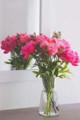 Bouquet of beautiful pink peonies in a glass vase on a wooden table by the mirror