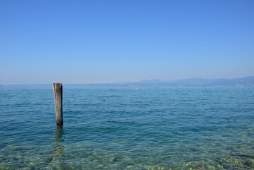 Fototapeta premium Holzpfahl im Wasser als Anlegestelle für Boote und Schiffe am Gardasee in den Sommermonaten 