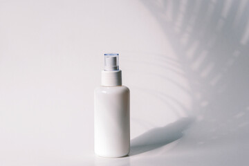 Cosmetic tonic in blank packages on a background of white wall with palm leaves shadow.