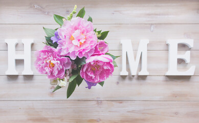 Letters HOME and  bouquet with pink peonies on a wooden table