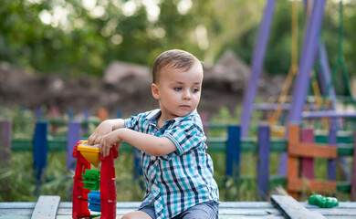 A child plays in the playground with toys in the sandbox. Toddler boy plays in the sand in the summer. Cheerful children's vacation outside.