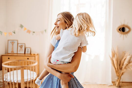 Young mother or babysitter with a little girl in her arms spin in the middle of the room