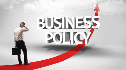 Fototapeta premium Rear view of a businessman standing in front of BUSINESS POLICY inscription, successful business concept