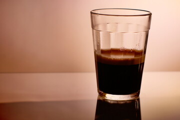 Transparent glass cup containing pure black coffee, on a light background. 