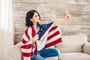 Lifestyle portrait of happy young woman taking selfie with American Flag by phone on July 4th, Independence Day