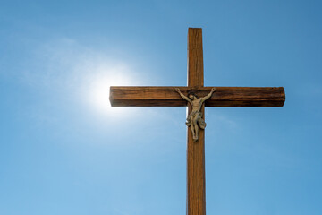 An old wooden Catholic cross against the background of the sun and clear blue sky. Religion and service to God as a path to redemption from sin. The face of Jesus crucified on the cross.
