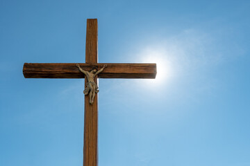 An old wooden Catholic cross against the background of the sun and clear blue sky. Religion and service to God as a path to redemption from sin. The face of Jesus crucified on the cross.