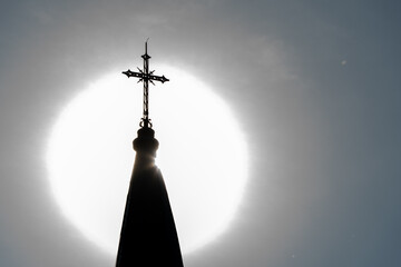 The cross on the spire of the church against the background of the sun. The halo of the sun beautifully frames the cross of the church.