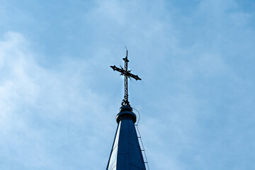 The cross on the spire of the church against the background of the sun and clear sky on a warm summer day. The cross as a symbol of faith in God.