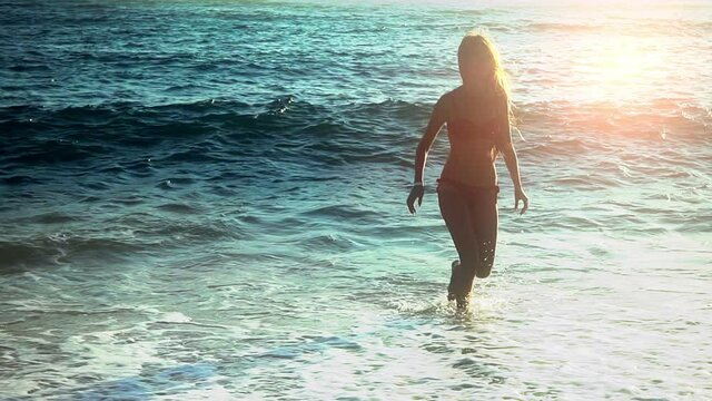 Beach vacation of girl barefoot comes out of sea from foam wave. Slow motion.