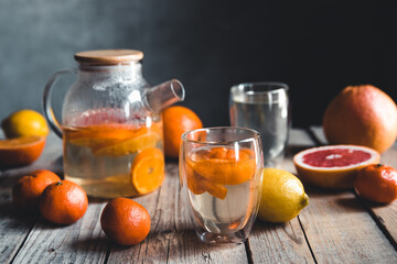 Citrus tea in a transparent teapot on a table with grapefruit and on a wooden table. Healthy drink.