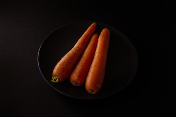 zanahorias frescas naturales en un plato negro sobre fondo negro