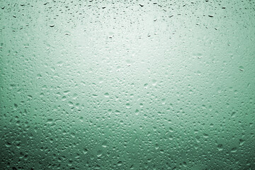 Drops of rain on a window glass with very diffuse landscape bluish green color