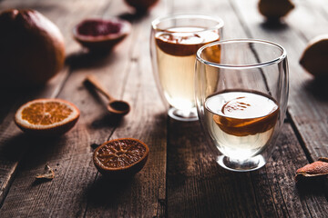 Citrus tea in a transparent teapot and a glass, healthy drink on a wooden background.