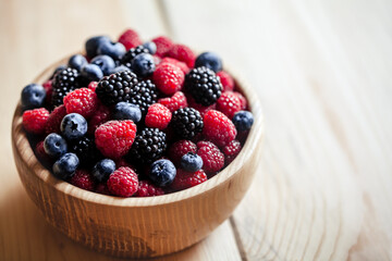 blueberries and raspberries, blackberry in a wooden bowl on old wood background