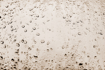 High contrast photo of drops of rain on a window glass with golden yellow color