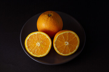 naranjas frescas cortadas en un plato negro sobre fondo negro