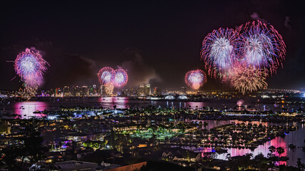 Independence day with many coordinated fireworks reflecting in the water in San Diego California with the downtown skyline