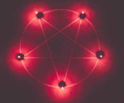 White pentagram symbol on concrete ground. Illuminated with candles. Dark background. Scary, mystical occultism.