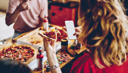Curly woman with piece of pizza and browsing smartphone