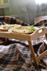 Yummy romantic breakfast in bed on bamboo food-tray on cosy checkered plaid. Omelette with fresh salat. Health food concept. Stay at home during quarantine. Save lives