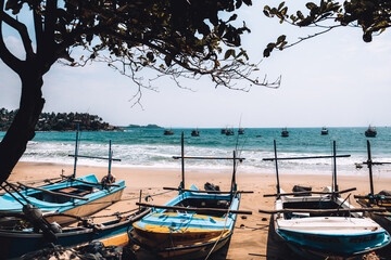 Idle fishing boats tied to the shore at a secluded beach in Sri Lanka. Blue ocean, windy weather...