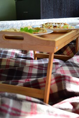 Yummy romantic breakfast in bed on bamboo food-tray on cosy checkered plaid. Omelette with fresh salat. Health food concept. Stay at home during quarantine. Save lives