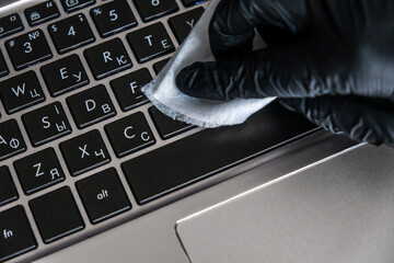 Cleaning the laptop keyboard with antibacterial wet wipes. Black glove and white napkin on a black computer. Removing dust and killing bacteria with hand sanitizer. Personal protection in quarantine.