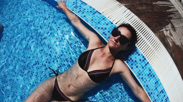 Young brunette woman in swimsuit. Girl relaxing and getting tan in swimming pool. Summer, traveling, resort and vacation concept.