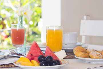 breakfast table with orange juice, watermelon, grapes, bread and coffee