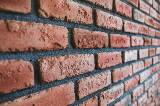 Side angle of a red brick wall. Close up view of cracked weathered cemented brickwork material. Modern interior design, unique perspective. Loft like room style at home. Rusty facade architecture.