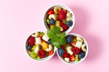 Fresh fruit salad on white bowl. Mixed fruit in white bowl healthy food style. Useful fruit salad of fresh fruits and berries on pink background. three bowls with fruit salad
