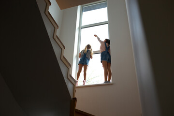 Two little girls standing on windowsill near stairs