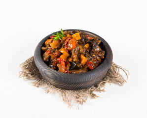Grilled vegetables in a wooden bowl, zucchini, eggplant, tomatoes, carrots, onions with pepper and garlic on a light background