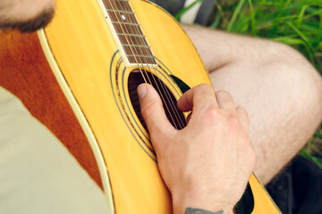 male hand fingers on acoustic guitar strings playing music for fun outside