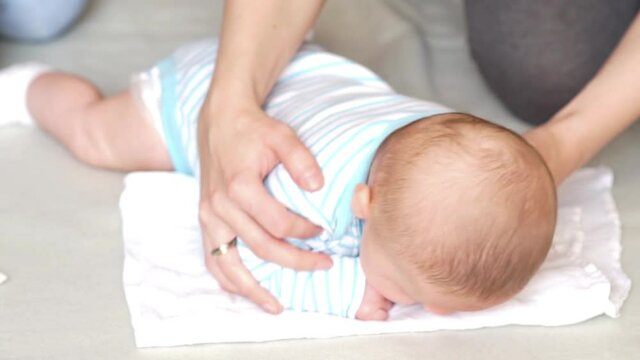 Woman physiotherapist helps little baby boy to lift and hold his head up while lying down on belly. Baby exercises - flat head prevention.