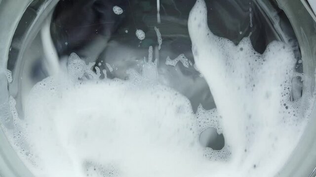 White washing machine washes dirty colorful clothes. Washing clothing in domestic washing machine. Close up video of spinning drum washing machine.